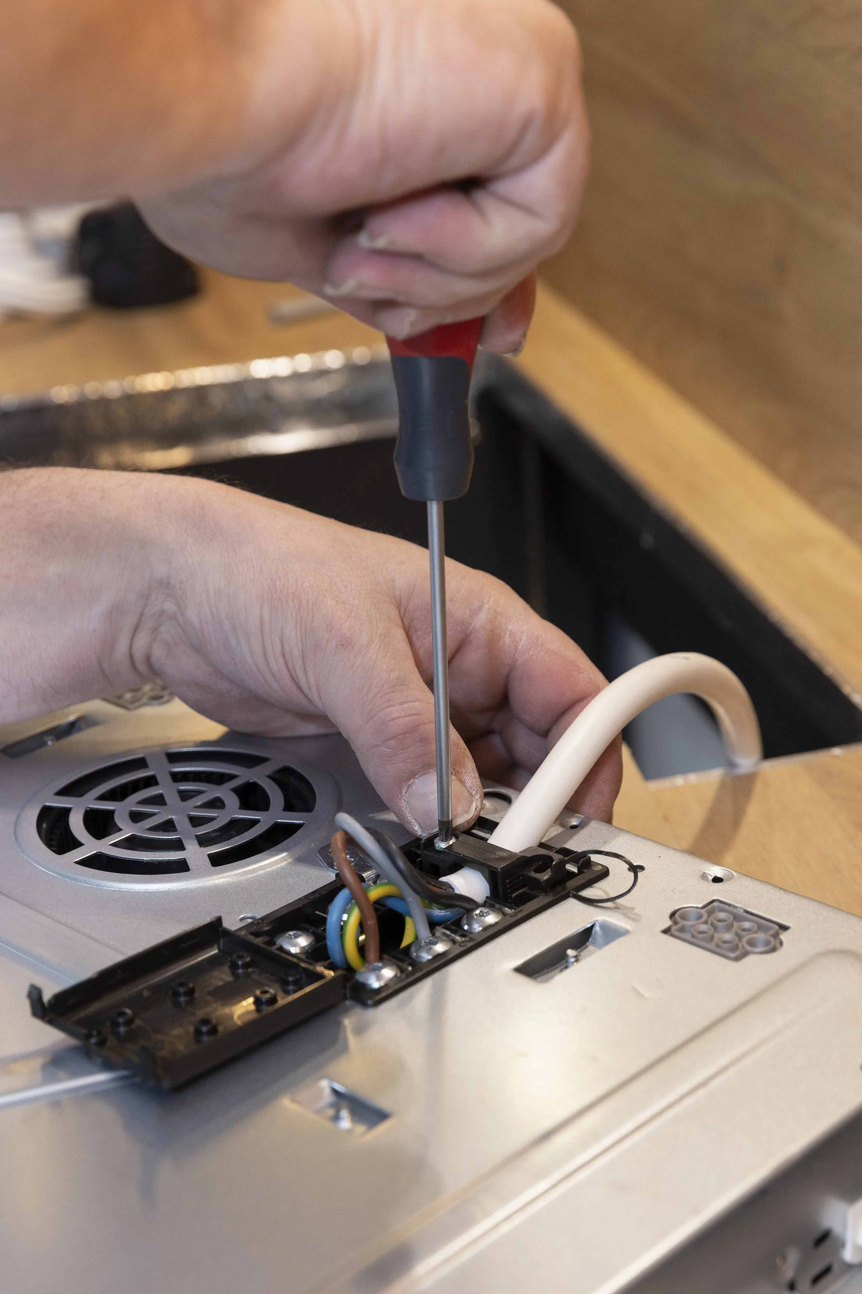 Hand schraubt Kabel an ein elektrisches Gerät fest