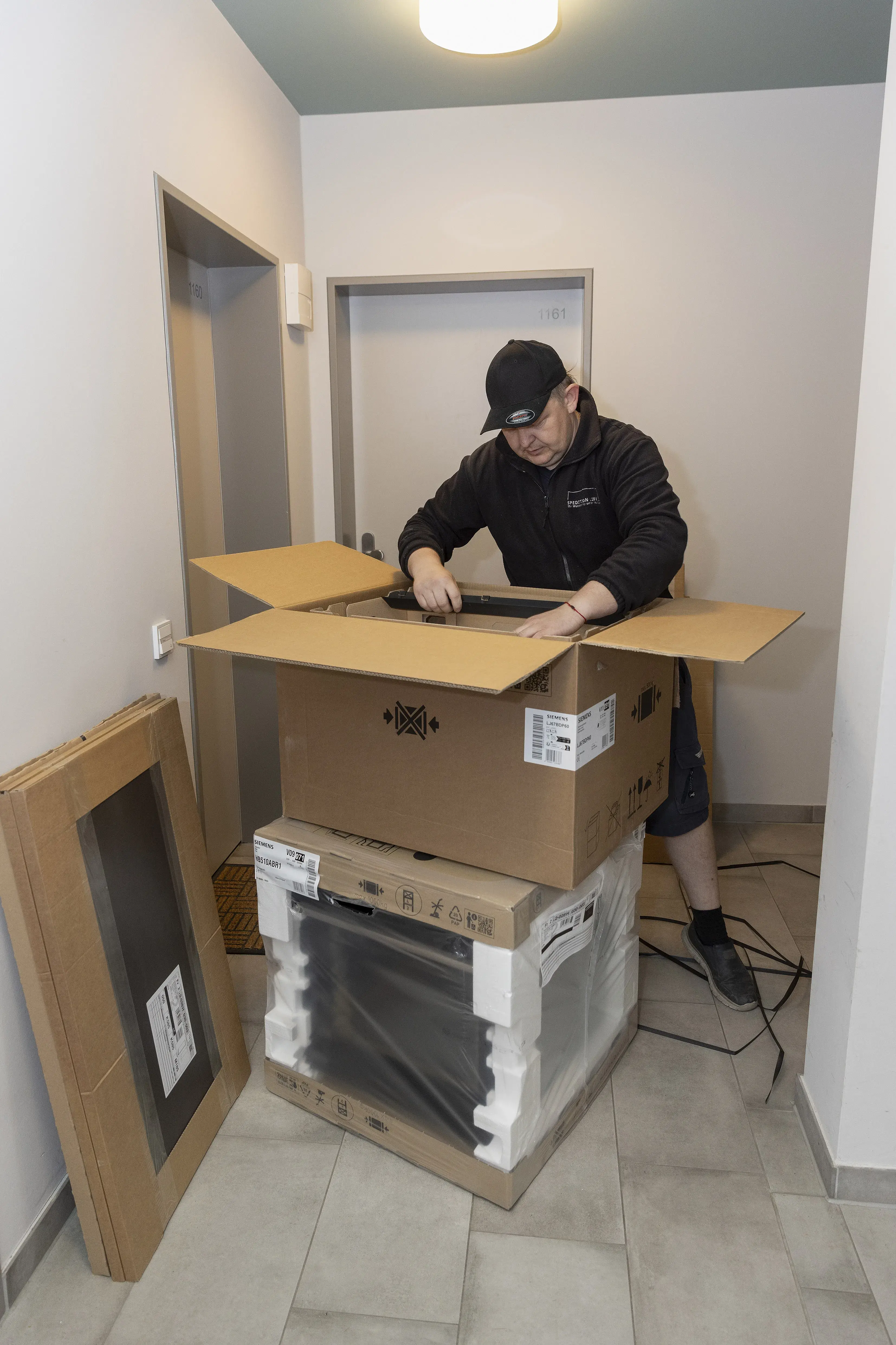 Mann packt in Flur einen neuen Haushaltsherd aus Kartons aus.